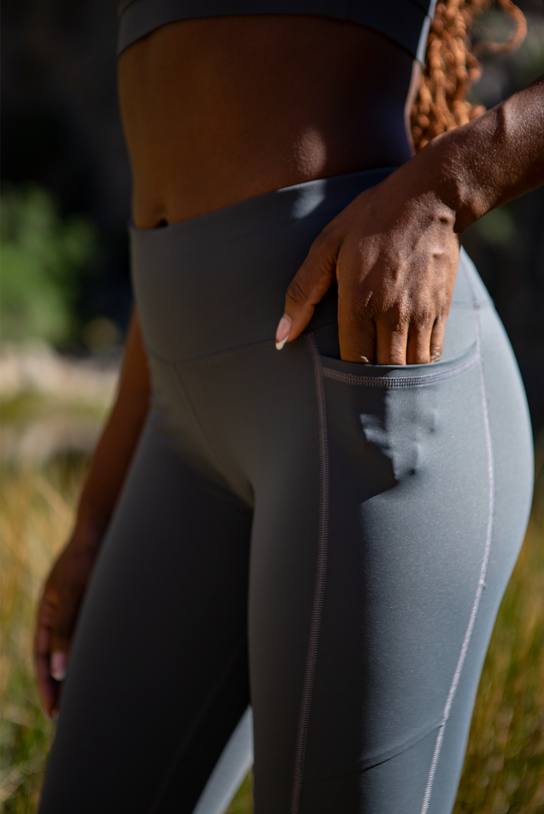 Close-up of a Black woman's hand resting on her hip, showcasing the detail of her MINKE Grey Set from NAUTRA. The image highlights the fabric's texture and the suit's craftsmanship, set against a natural, outdoor backdrop.